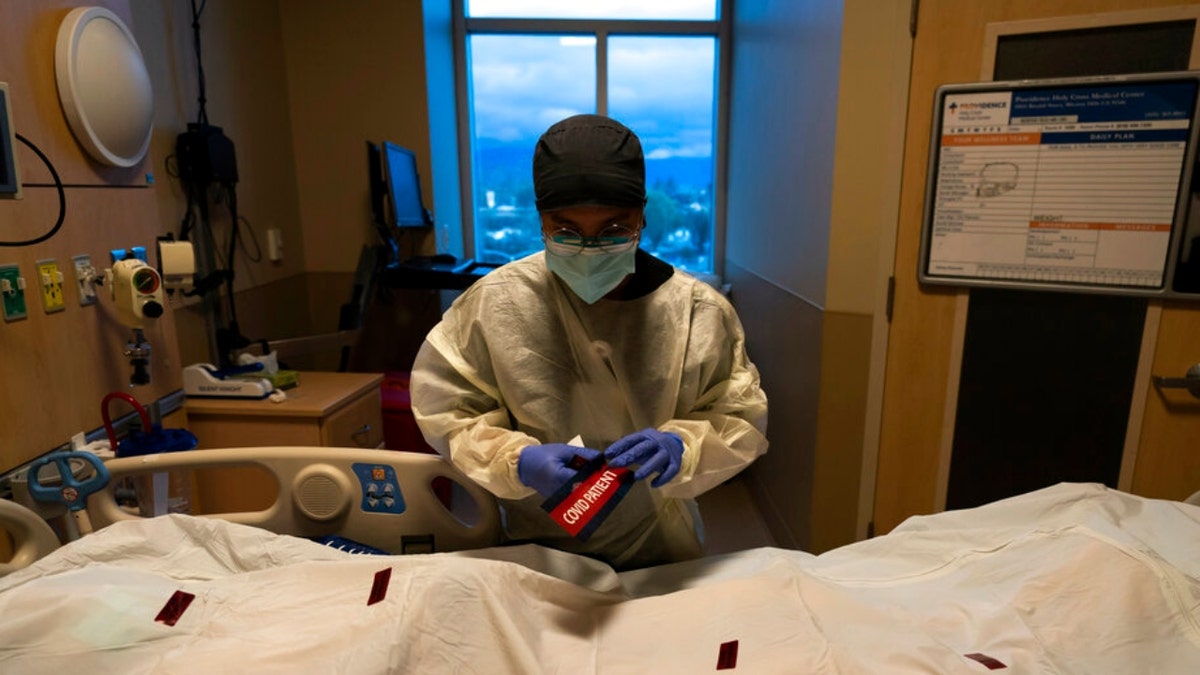 Registered nurse Bryan Hofilena attaches a "COVID Patient" sticker on a body bag of a patient who died of coronavirus at Providence Holy Cross Medical Center in Los Angeles, Tuesday, Dec. 14, 2021. 