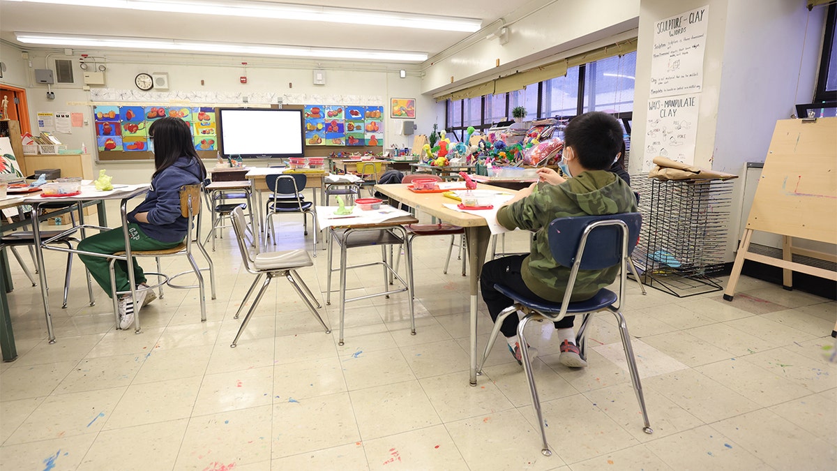 elementary school students sitting at desks in mostly empty classroom