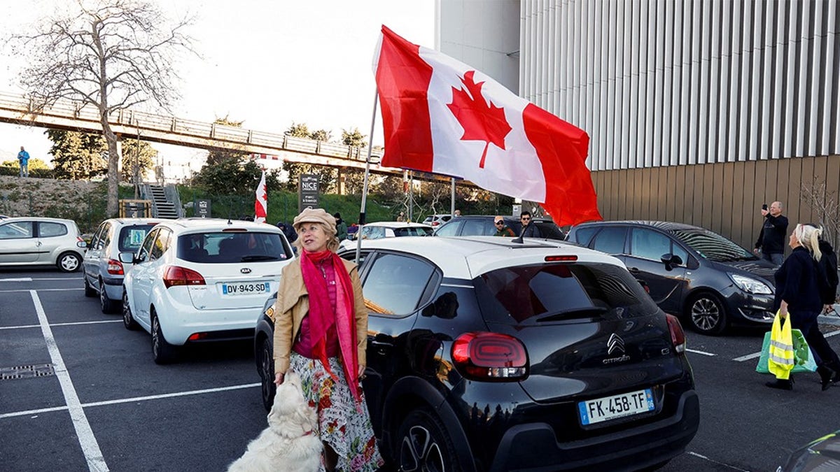 A woman and her dog stand by a Canadian flag before the start of their "Convoi de la liberte" (The Freedom Convoy), a vehicular convoy protest converging on Paris to protest coronavirus disease (COVID-19) vaccine and restrictions in Nice, France, February 9, 2022. 