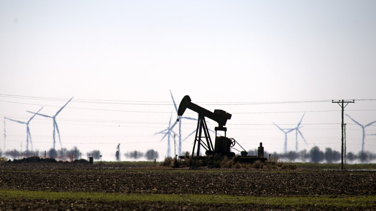 An oil pump jack in a field with wind turbines in Corpus Christi, Texas, U.S., Friday, Feb. 19, 2021. 