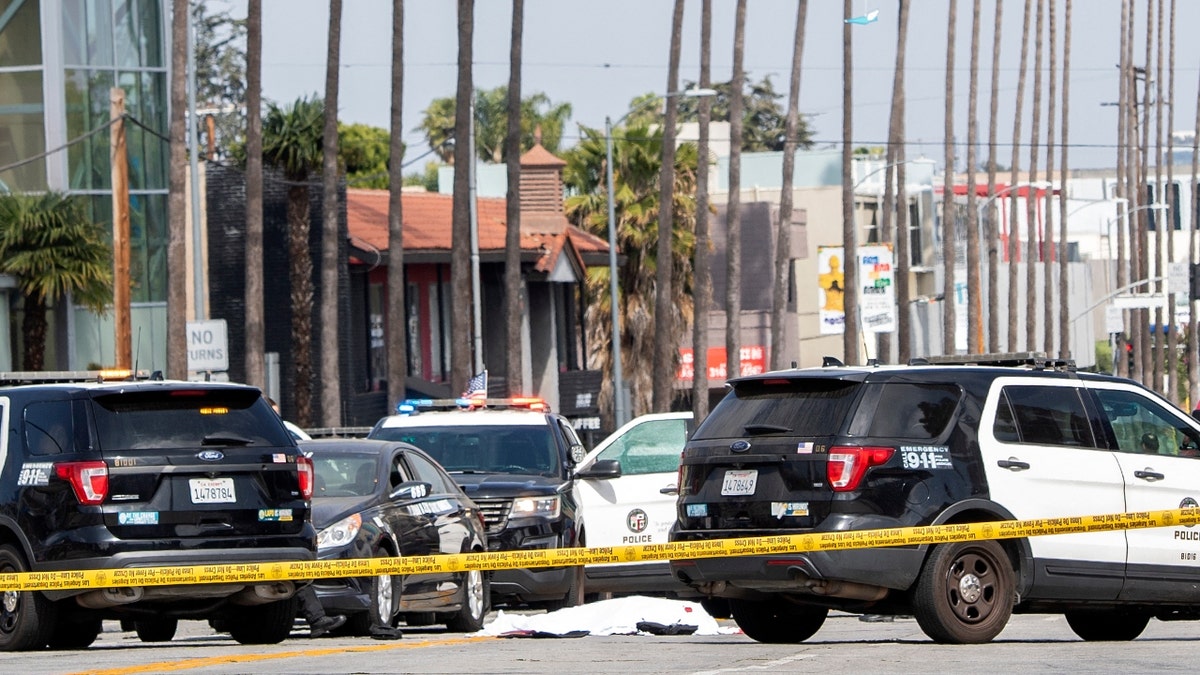 A LAPD police officer stands at the corner of Fairfax Avenue and Sunset Boulevard where a body covered in a white sheet lies on the pavement in Los Angeles on April 24, 2021 in what appears to be an officer-involved shooting. (Photo by VALERIE MACON / AFP) (Photo by VALERIE MACON/AFP via Getty Images)