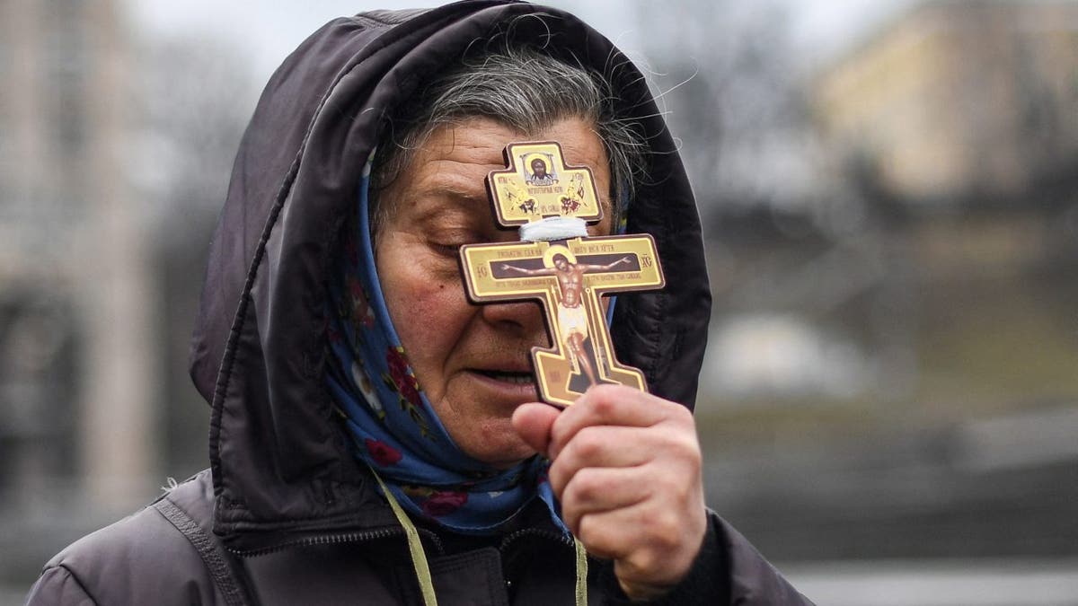 A religious woman holds a cross as she prays on Independence square in Kyiv in the morning of February 24, 2022.