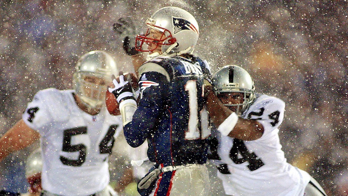 New England Patriots  quarterback Tom Brady (C) takes a hit from Charles Woodson (R) of the Oakland Raiders on a pass attempt in the last two minutes of the game in their AFC playoff 19 January 2002 in Foxboro, Massachusetts. The Patriots won 16-13 in overtime.