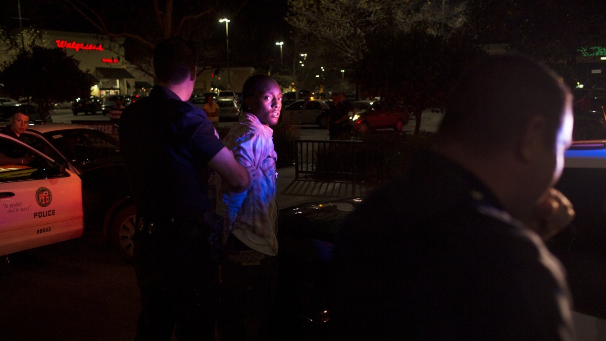 Unidentified Los Angeles Police Department officers move a handcuffed man to a patrol car after he and another man, far left, tried to outrun the police after a LAPD patrol car attempted to pull the suspects over in downtown Los Angeles, California January 30, 2013. Both men were arrested. The car's driver was charged with evading the police while in pursuit and the passenger was found with an outstanding arrest warrant on him. (Photo by Robert Nickelsberg/Getty Images)