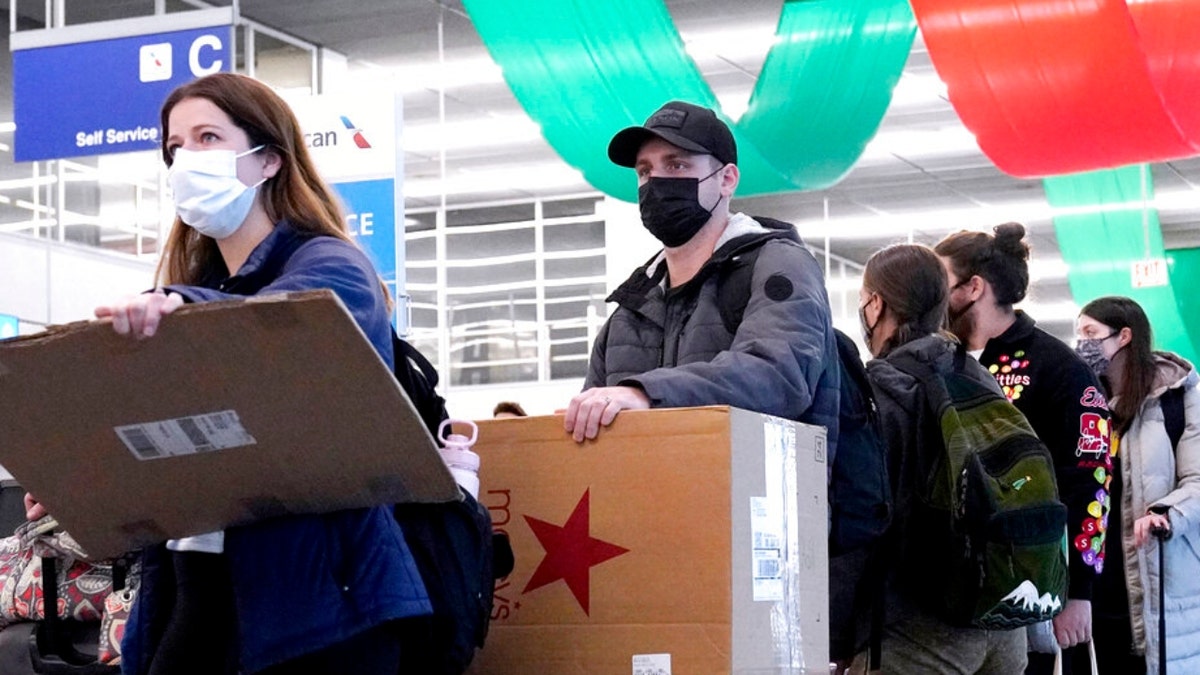 Travelers line up wearing protective masks indoors at O'Hare International Airport in Chicago, Tuesday, Dec. 28, 2021. 