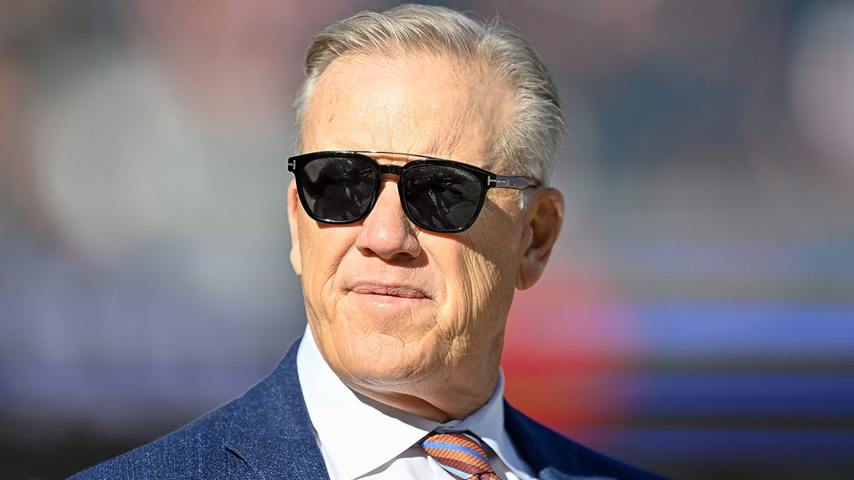 John Elway, president of football operations for the Denver Broncos, stands on the field before a game between the Broncos and the Cincinnati Bengals at Empower Field at Mile High on Dec. 19, 2021, in Denver, Colorado.