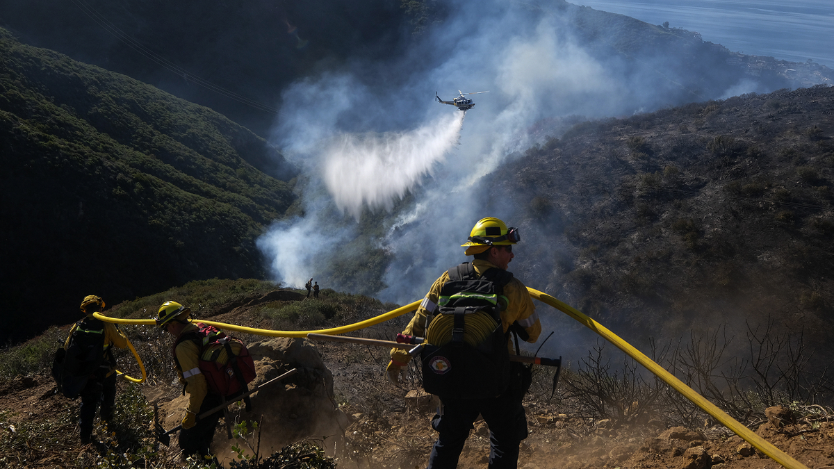 Firefighters watch as a helicopter drops water on the Emerald Fire Thursday in Laguna Beach, Calif. 