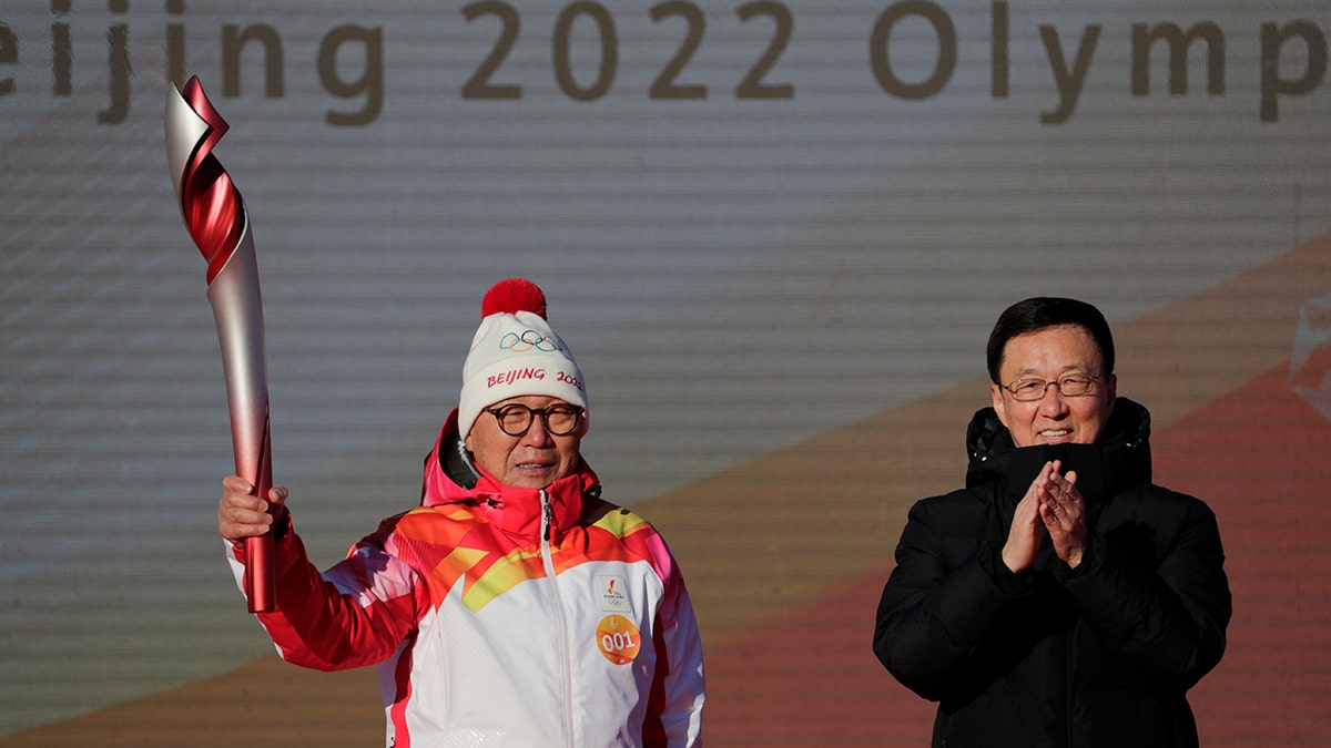First Torch bearer Luo Zhihuan holds up the torch after receiving it from Chinese Vice Premier Han Zheng before the start of the torch relay for the 2022 Winter Olympics at the Olympic Forest Park in Beijing on Wednesday, Feb. 2, 2022.