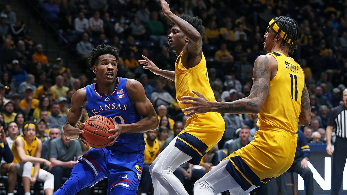 Kansas guard Ochai Agbaji, left, is defended by West Virginia guard Kedrian Johnson, center, and forward Jalen Bridges during the first half of an NCAA college basketball game in Morgantown, W.Va., Saturday, Feb. 19, 2022. 