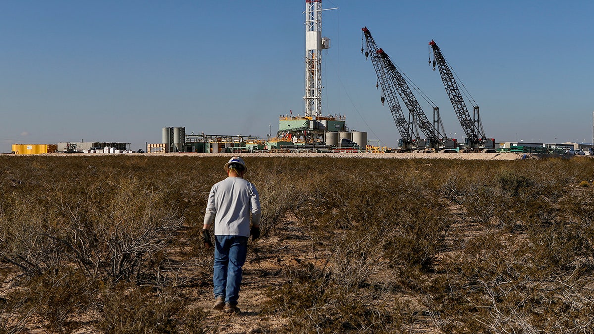 An oil worker walks toward a drill rig after placing ground monitoring equipment in the vicinity of the underground horizontal drill in Loving County, Texas, U.S.