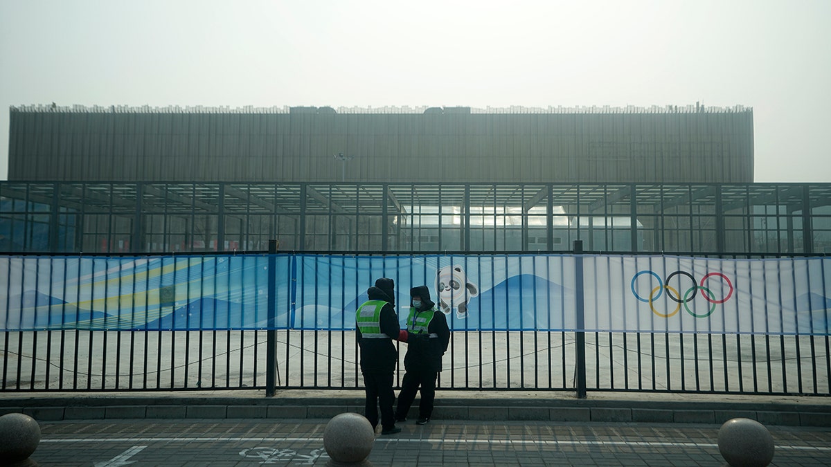Security personnel stand on the sidewalk near Wukesong Sports Centre hockey venue ahead of the 2022 Winter Olympics, Sunday, Jan. 30, 2022, in Beijing.
