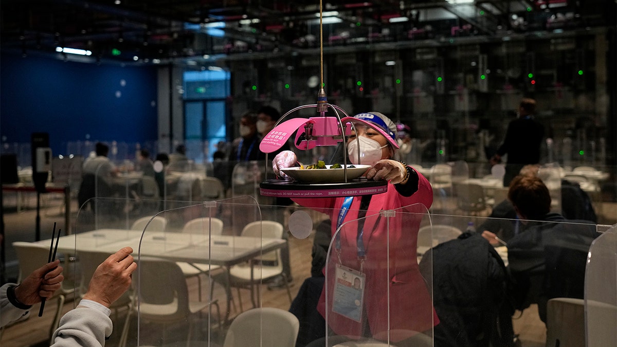 A worker grabs food delivered to a table robotically in the media dining area of the main media center ahead of the 2022 Winter Olympics, Wednesday, Feb. 2, 2022, in Beijing. 