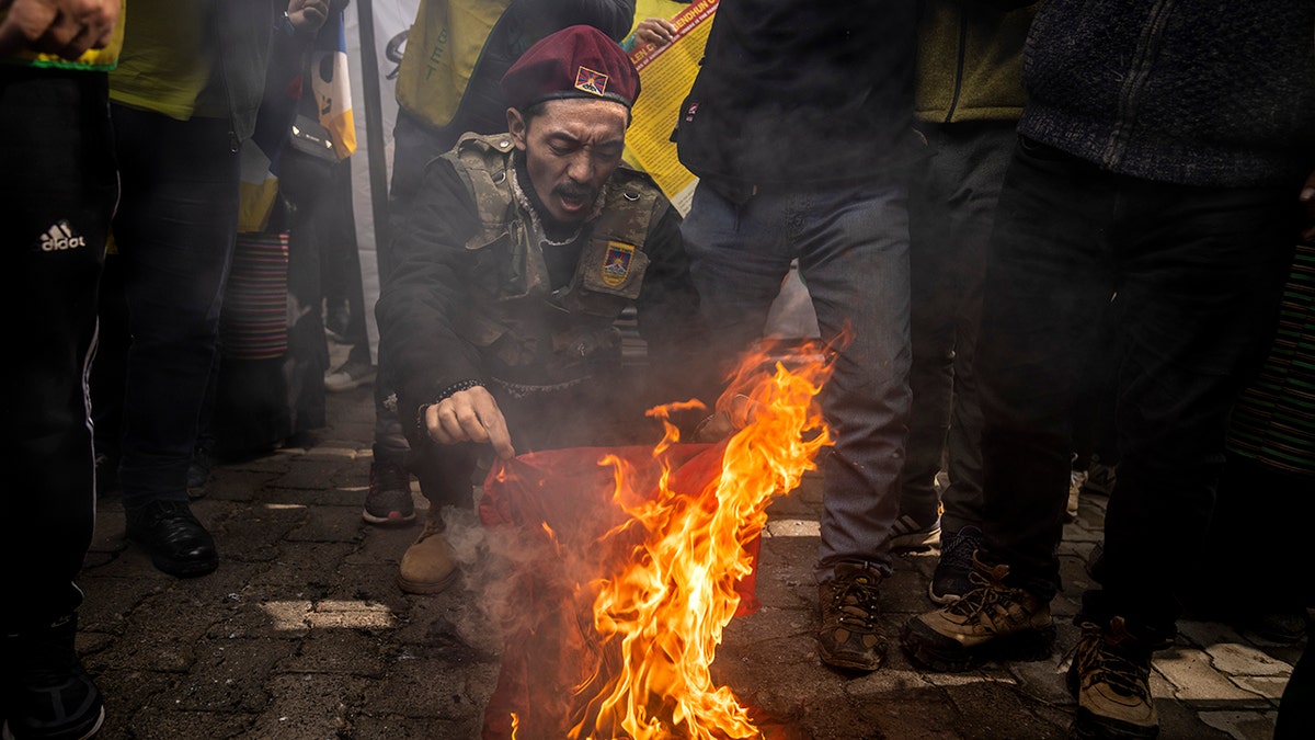An exile Tibetan holds a burning Chinese flag during a protest against Beijing Winter Olympic Games in New Delhi, India, Friday, Feb. 4, 2022. Hundreds of Tibetan exiles are marching outside the Chinese Embassy in New Delhi, denouncing the Beijing Winter Olympics and demanding freedom for their region.