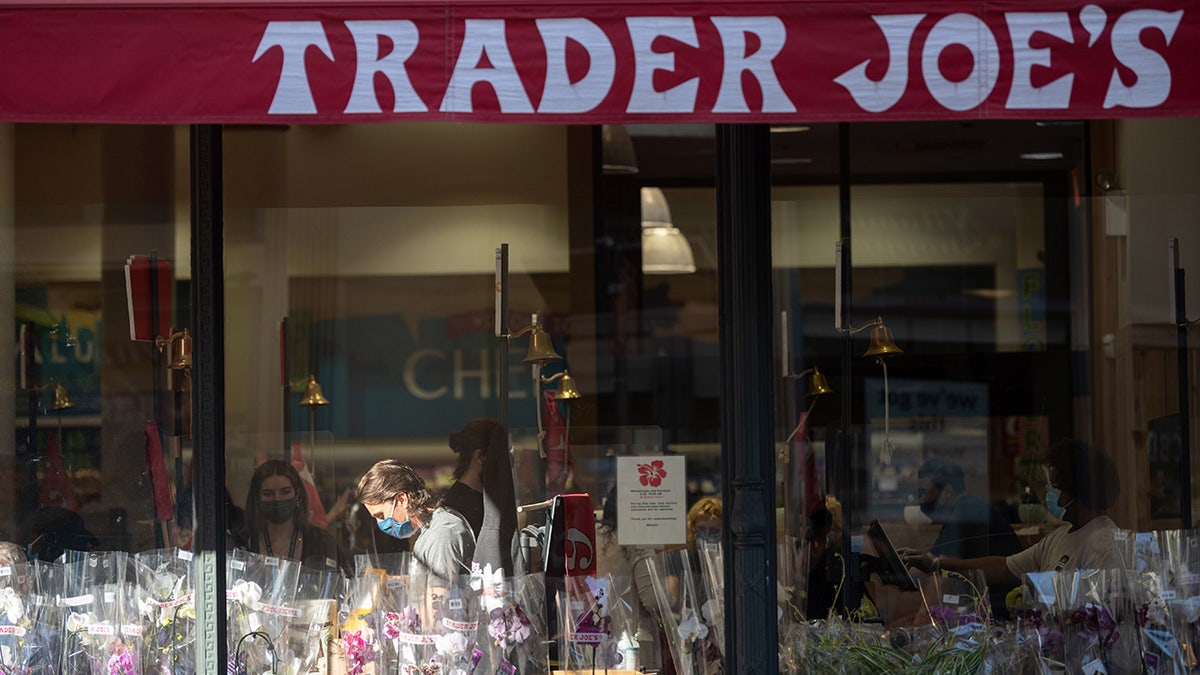 An employee is seen through a window working a register in a patch of sunlight at Trader Joe's in New York City's Chelsea neighborhood. 