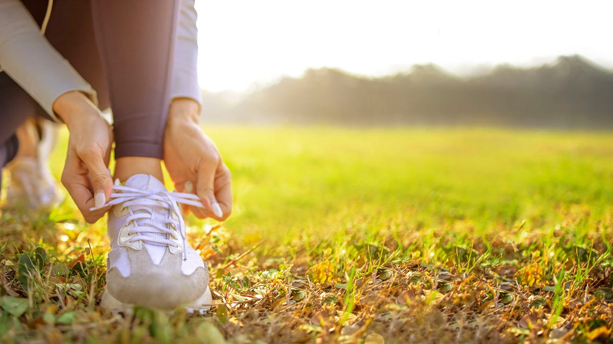 young woman runner tying her shoes preparing for a jog outside at morning