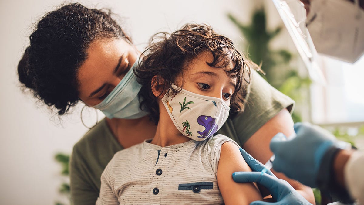 A child is given a vaccine while he and his mother wear a mask