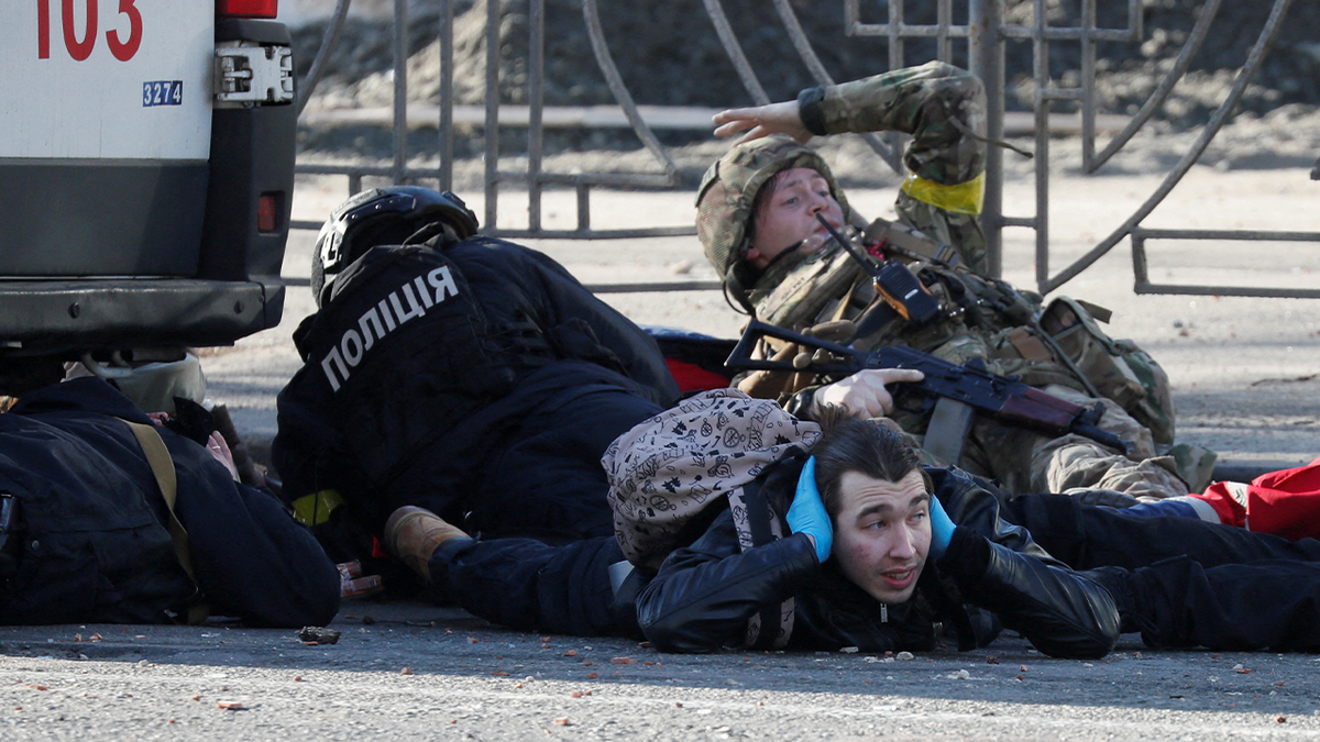 People take cover as an air-raid siren sounds near an apartment building damaged by recent shelling in Kyiv, Ukraine, Feb. 26, 2022. 