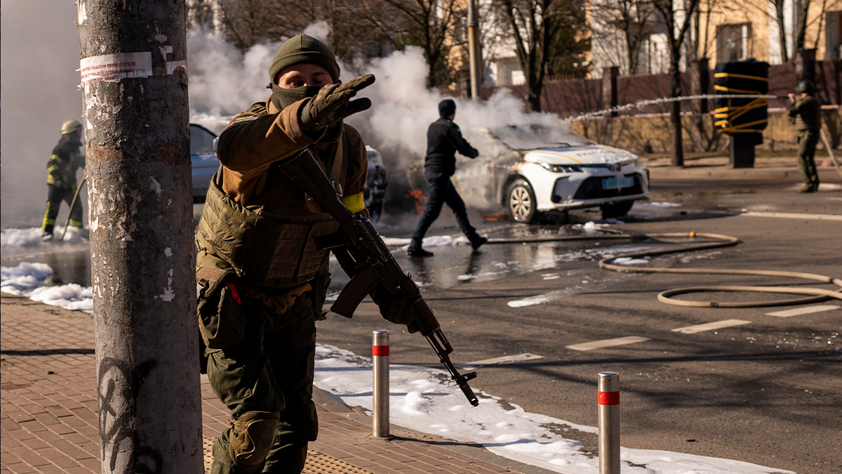 Ukrainian soldiers take positions outside a military facility as two cars burn, in a street in Kyiv, Ukraine, Saturday, Feb. 26, 2022.