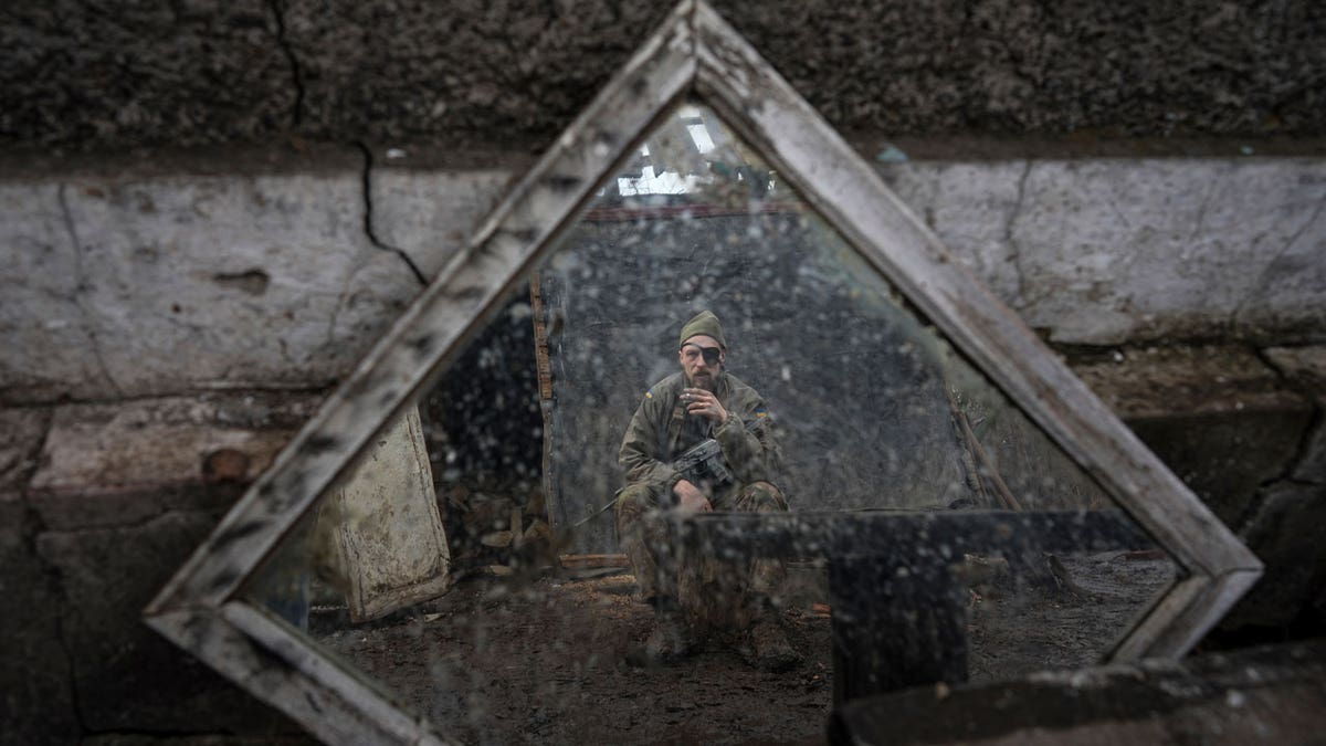 A Ukrainian serviceman is reflected in a mirror as he smokes a cigarette on a position at the line of separation between Ukraine-held territory and rebel-held territory near Zolote, Ukraine, Saturday, Feb. 19, 2022.