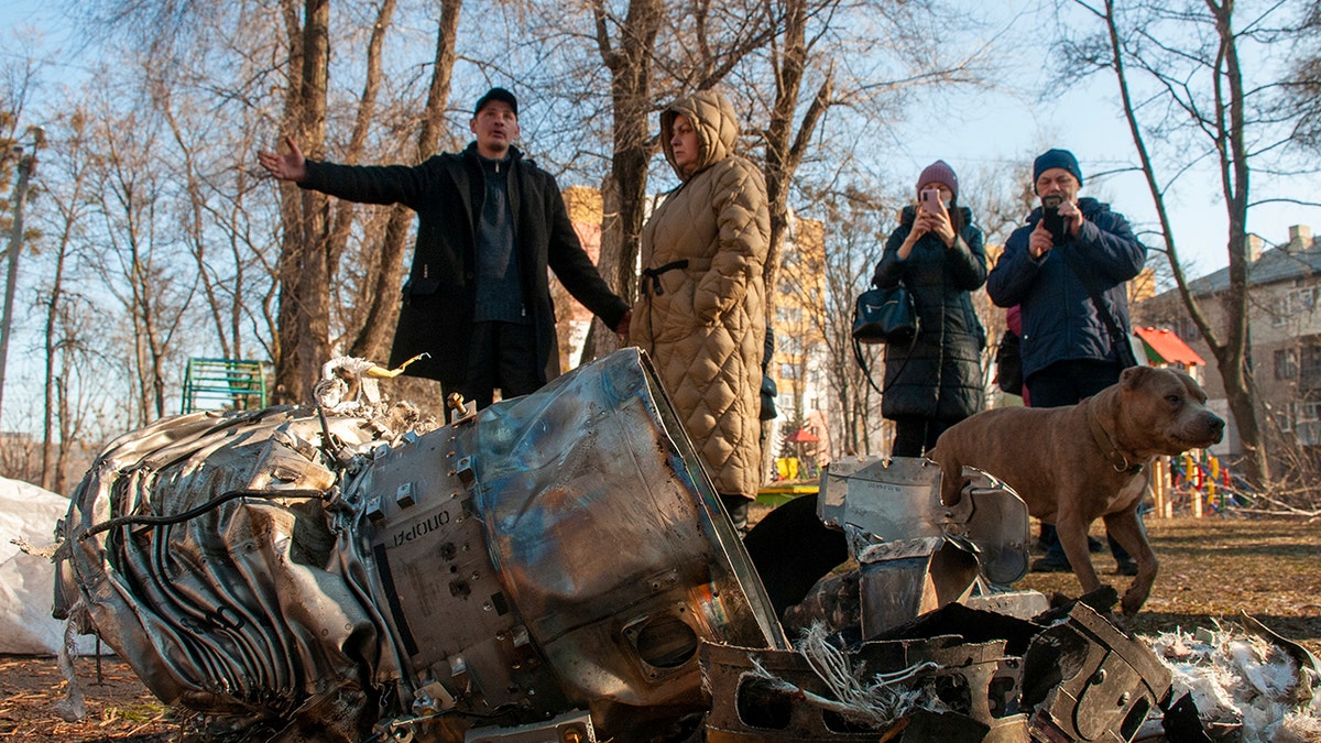 People stand next to fragments of military equipment on the street in the aftermath of an apparent Russian strike in Kharkiv in Kharkiv, Ukraine, Thursday, Feb. 24, 2022. 