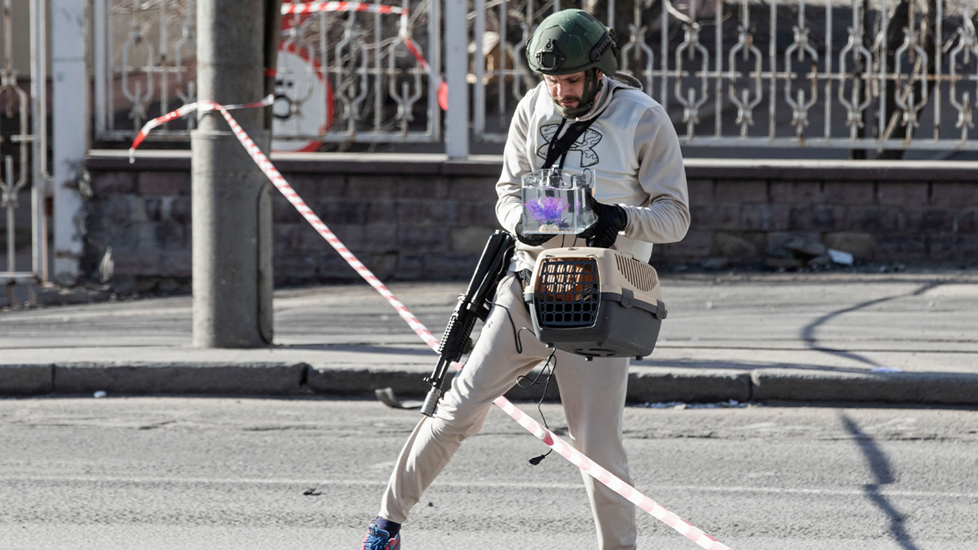 An armed local resident carries a cat in a carrier and a fish in an aquarium, which he took out of an apartment building damaged by recent shelling in Kyiv, Ukraine February 26, 2022.
