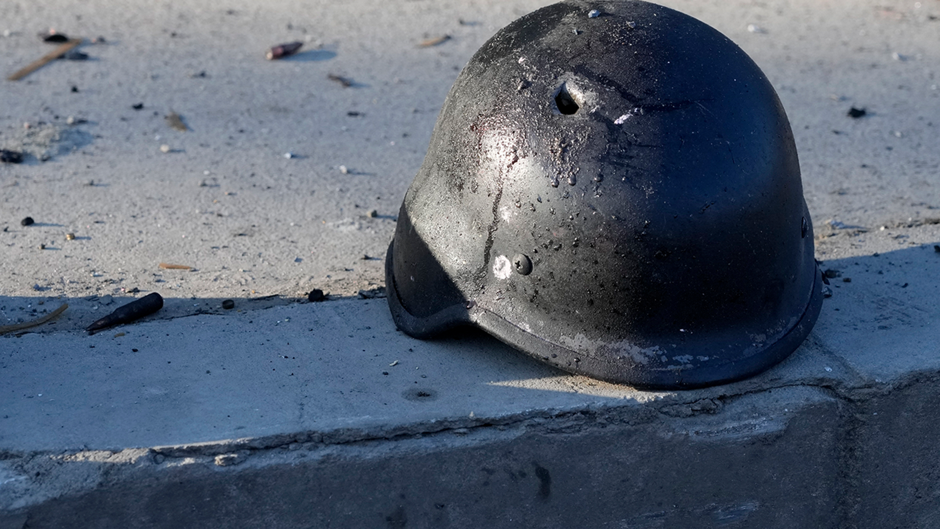 A soldier's helmet with a bullet hole near debris of burning military trucks, in a street in Kyiv, Ukraine, Saturday, Feb. 26, 2022. Russian troops stormed toward Ukraine's capital Saturday, and street fighting broke out as city officials urged residents to take shelter
