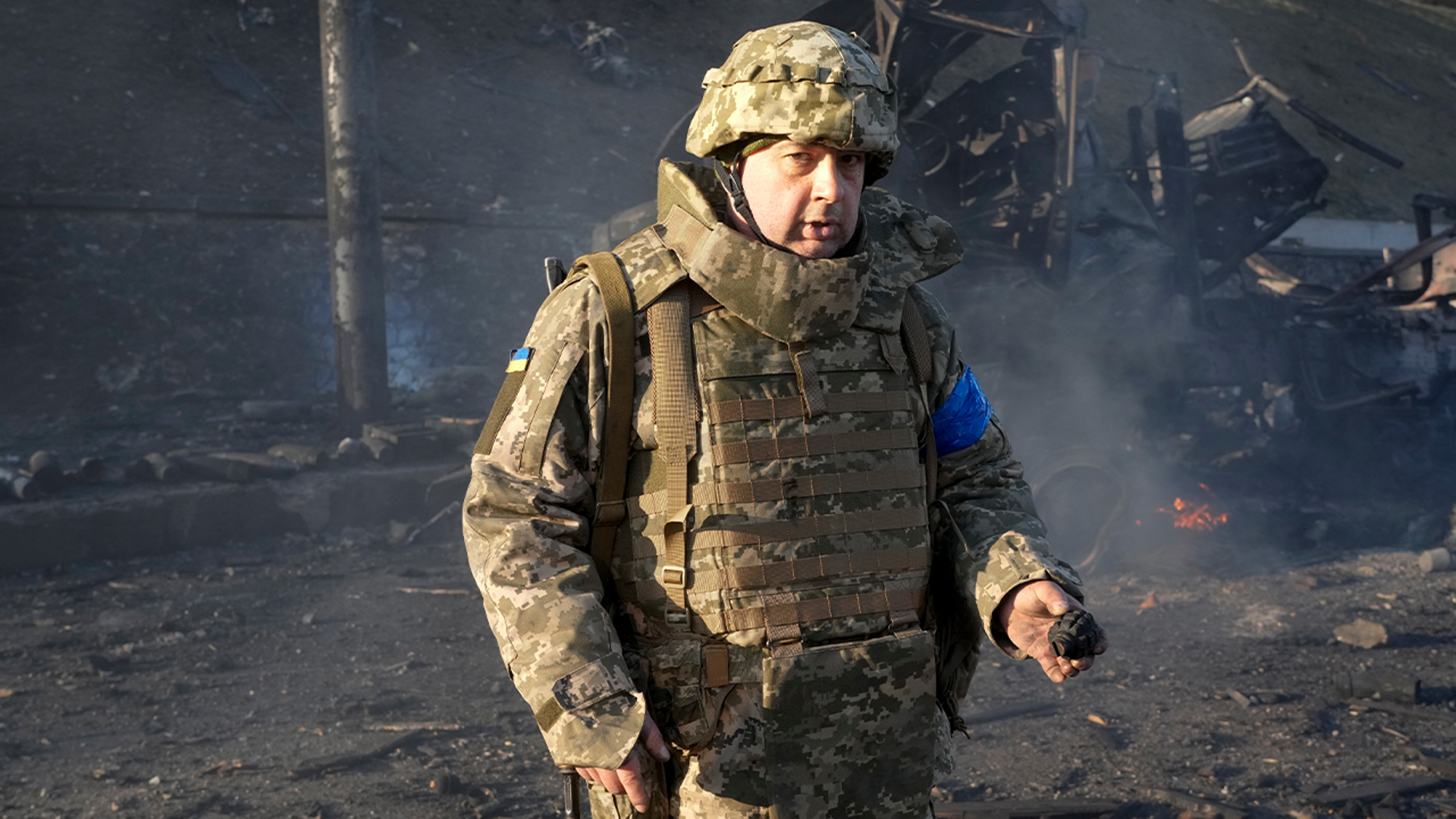 A Ukrainian soldier shows a grenade, near burning military trucks in a street in Kyiv, Ukraine, Saturday, Feb. 26, 2022. Russian troops stormed toward Ukraine's capital Saturday, and street fighting broke out as city officials urged residents to take shelter.