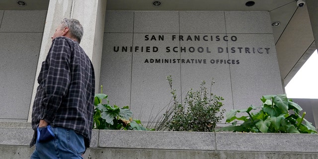A pedestrian walks past a San Francisco Unified <a class=