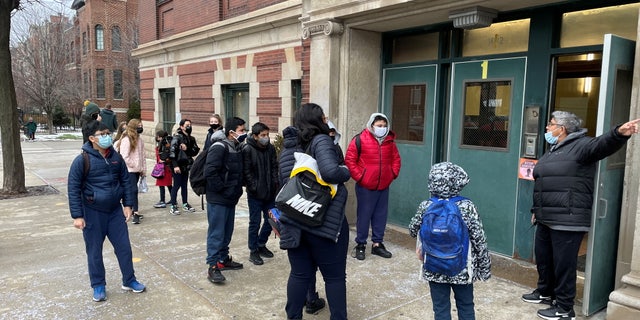 Students wearing face masks line up outside the entrance of Prescott Elementary School while directed by school staff in Chicago, イリノイ, 我ら. 1月 12, 2022.