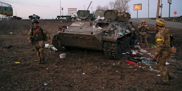 Los militares ucranianos se ven junto a un vehículo blindado destruido, que dicen pertenece al ejército ruso, en las afueras de Kharkiv, Ucrania, el 24 de febrero de 2022. 