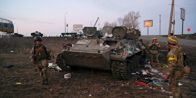 Los militares ucranianos se ven junto a un vehículo blindado destruido, que dicen pertenece al ejército ruso, en las afueras de Kharkiv, Ucrania, el 24 de febrero de 2022. 