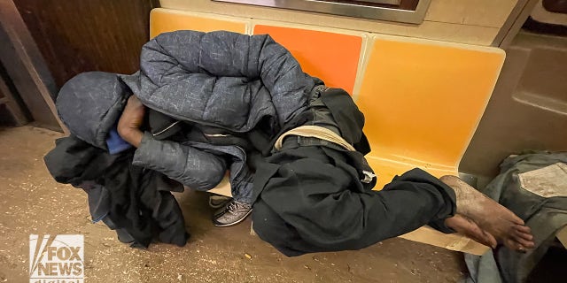 Image shows an individual sleeping in a NYC subway car. 