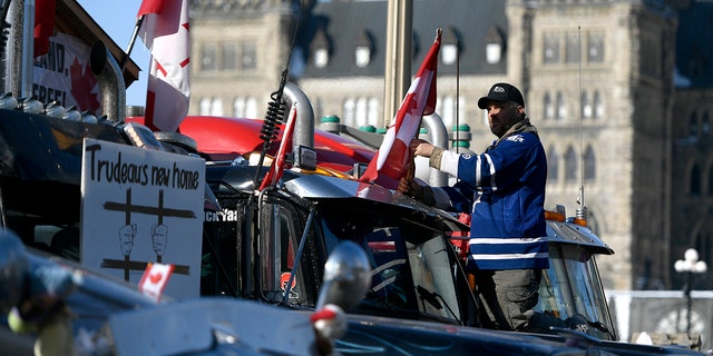 A protester affixes a flag to the top of a truck, parked beside another with a sign calling for the jailing of Prime Minister Justin Trudeau on Feb. 7, 2022