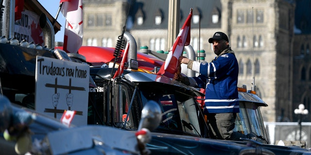 A protester affixes a flag to the top of a truck, parked beside another with a sign calling for the jailing of Prime Minister Justin Trudeau, outside Parliament Hill, as a protest against COVID-19 restrictions continues into its second week in Ottawa on Monday, Feb. 7, 2022. (Justin Tang/The Canadian Press via AP)