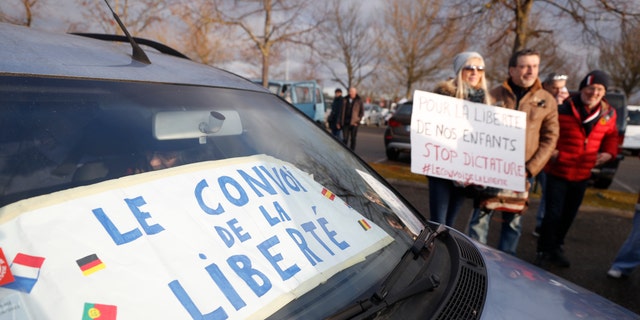 Protesters hold a placard next to car part of the "Freedom Convoy" and heading to Paris, Friday, Feb.11, 2022 in Strasbourg, eastern France. 