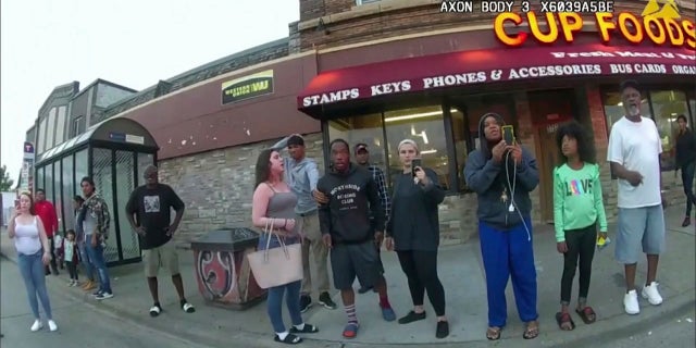 In this image from a police body camera, bystanders including Alyssa Funari, left filming, Charles McMillan, center left in light colored shorts, Christopher Martin center in gray, Donald Williams, center in black, Genevieve Hansen, fourth from right filming, Darnella Frazier, third from right filming, witness as then Minneapolis police officer Derek Chauvin pressed his knee on George Floyd's neck for several minutes, killing Floyd on May 25, 2020, in Minneapolis.