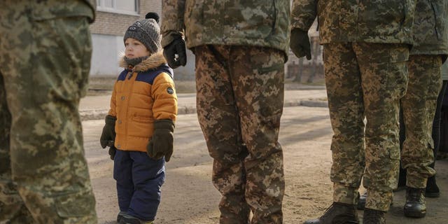 A child copies the posture of Ukrainian servicemen standing at attention during the national anthem during an event marking Unity Day in Sievierodonetsk, Luhansk region, eastern Ukraine, Wednesday, Feb. 16, 2022. 