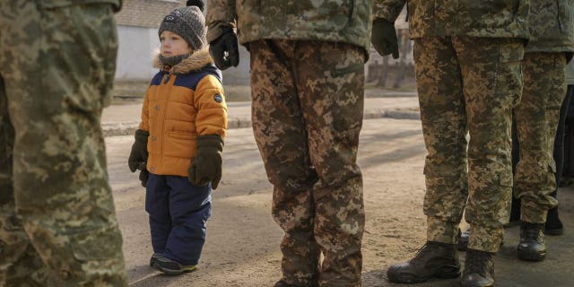 A child copies the position of Ukrainian servicemen standing at attention during the national anthem during an event marking a Day of Unity in Sievierodonetsk, the Luhansk region, eastern Ukraine, Wednesday, Feb. 16, 2022. 