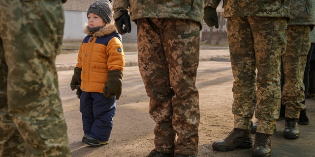 A child copies the position of Ukrainian servicemen standing at attention during the national anthem during an event marking a Day of Unity in Sievierodonetsk, the Luhansk region, eastern Ukraine, Wednesday, Feb. 16, 2022.