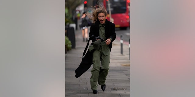A woman attending a fashion show at London Fashion Week reacts to the wind as she waits to enter the runway presentation in London, Friday, Feb. 18, 2022.
