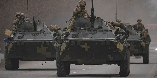 Ukrainian servicemen sit atop armored personnel carriers driving on a road in the Donetsk region