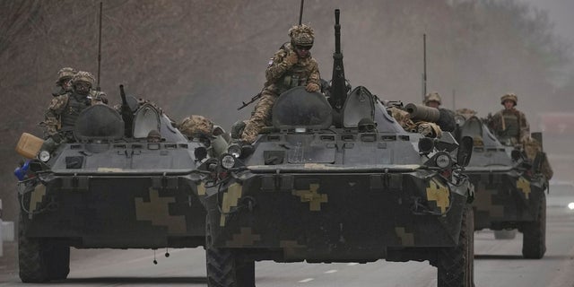 Ukrainian servicemen sit atop armored personnel carriers driving on a road in the Donetsk region