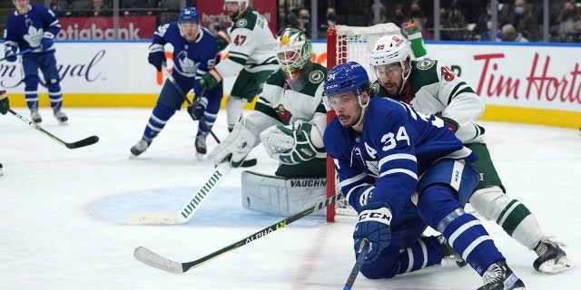 Toronto Maple Leafs center Auston Matthews (34) controls the puck to the side of Minnesota Wild goaltender Kaapo Kahkonen as Wild center Frederick Gaudreau (89) defends during the second period of an NHL hockey game Thursday, Feb. 24, 2022, in Toronto.