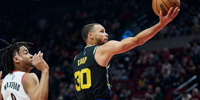 Golden State Warriors guard Stephen Curry, right, shoots in front of Portland Trail Blazers forward Trendon Watford during the first half of an NBA basketball game in Portland, Ore., Thursday, Feb. 24, 2022.