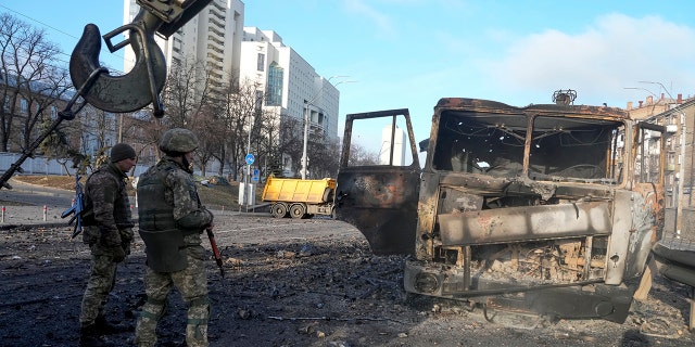 Ukrainian soldiers stand next to a burnt military truck, in a street in Kyiv, Ukraine, Saturday, Feb. 26, 2022. Russian troops stormed toward Ukraine's capital Saturday, and street fighting broke out as city officials urged residents to take shelter.