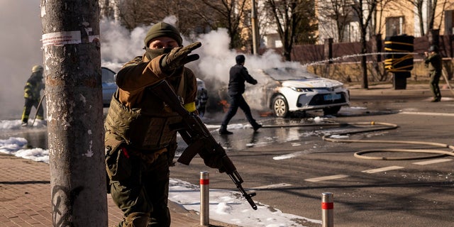 Ukrainian soldiers take positions outside a military facility as two cars burn, in a street in Kyiv, 우크라이나, 토요일에, 2 월. 26, 2022. 