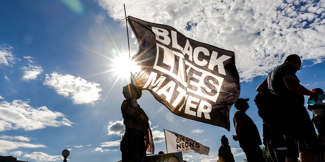 A woman holds a Black Lives Matter flag during an event in remembrance of George Floyd.