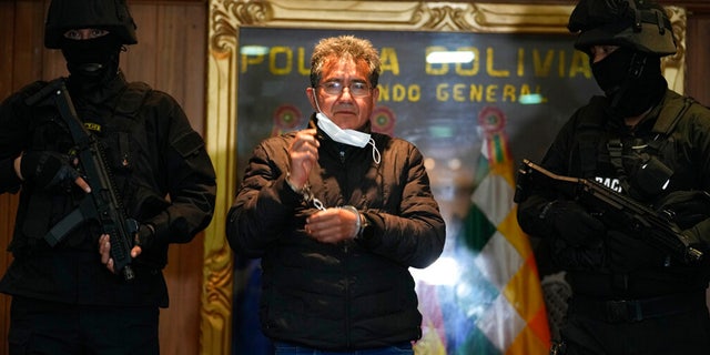 FILE: Police escort former police colonel Maximiliano Davila as he was presented to the media at a Bolivian Police Command office, in La Paz, Bolivia, Sunday, Jan. 23, 2022.