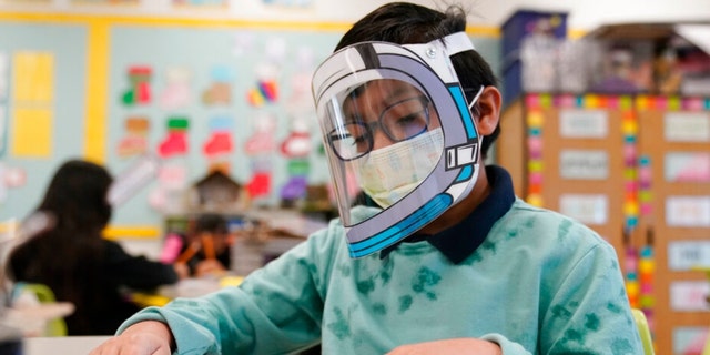 FILE - A student wears a mask and face shield in a 4th grade class amid the COVID-19 pandemic at Washington Elementary School on Jan. 12, 2022, in Lynwood, Calif. Gov. Gavin Newsom delayed a ly watched decision on lifting California's school mask mandate Monday, Feb. 14 even as other Democratic governors around the country have dropped them in recent weeks. (AP Photo/Marcio Jose Sanchez, File) 