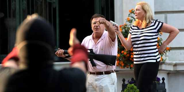 Armed homeowners Mark and Patricia McCloskey stand in front their house as they confront protesters marching to St. Louis Mayor Lyda Krewson's house on June 28, 2020.